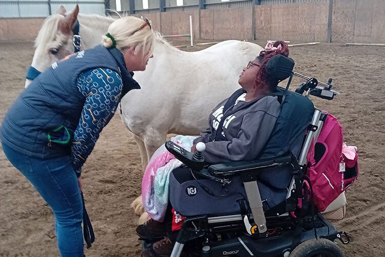 Girl in wheelchair site beside white horse.