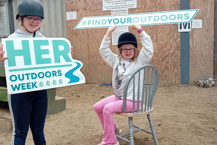 Two young girls hold signs for Her Outdoors Week.