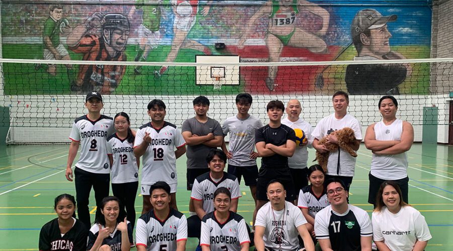 Group of men in pose for picture in front of a basketball and volleyball net.