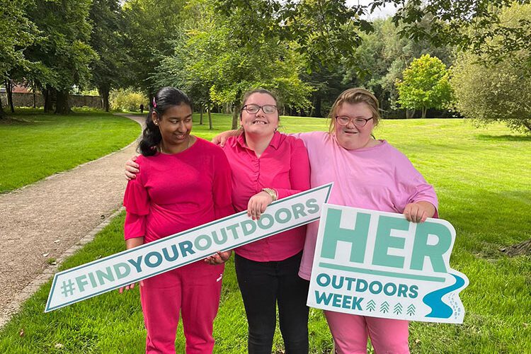 Three girls wearing pink hold signs for Her Outdoors Week when in park.