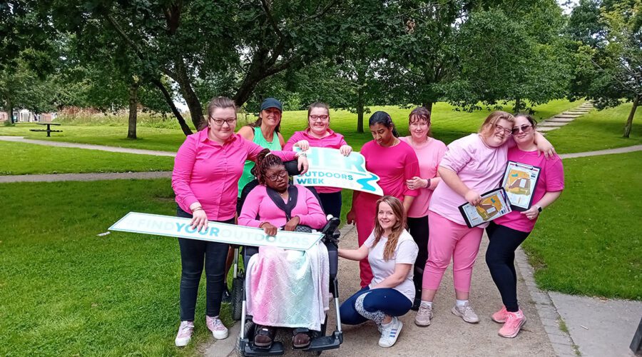 Group of young girls wearing pink hold signs for Her Outdoors Week when in park.