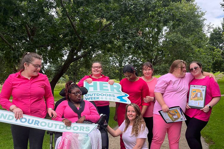 Group of young girls wearing pink hold signs for Her Outdoors Week when in park.