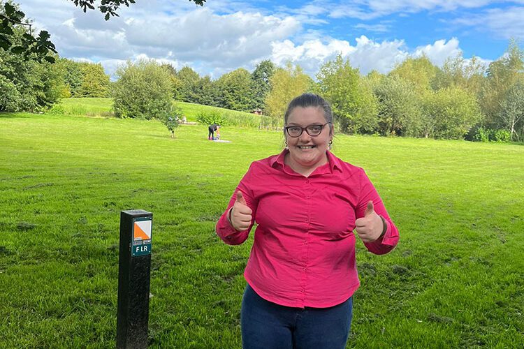 Teenage girl wearing pink holds up thumbs in a park.