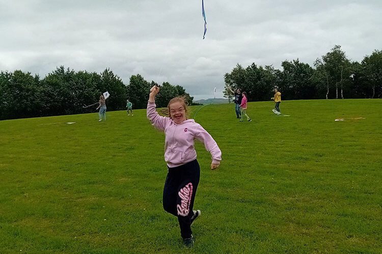 Young girl wearing pink flies kite in a park.