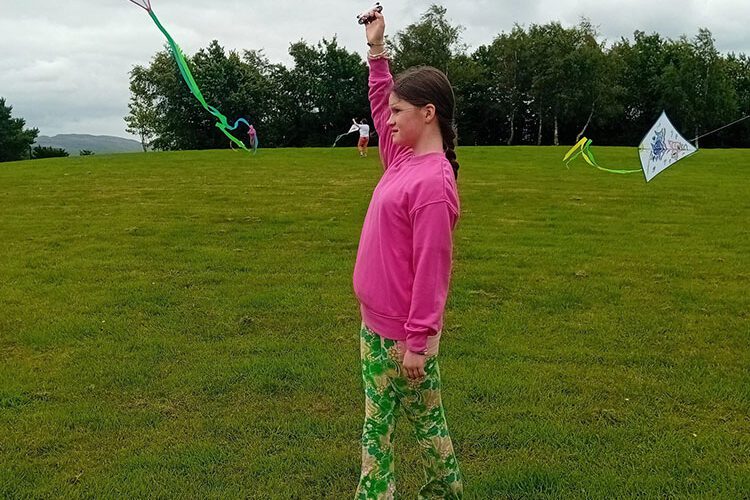 Young girl wearing pink flies kite in a park.