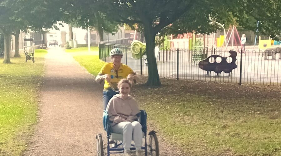 Two women cycle on a wheelchair accessible bicycle.