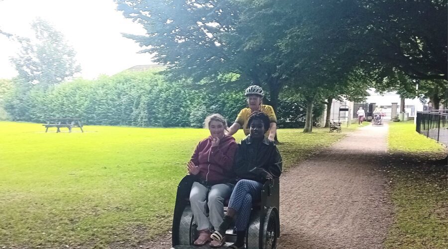 Two women on a push bike cycle through park for Come n' try in the park.