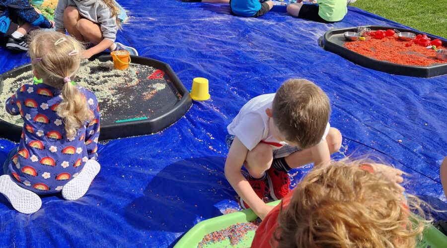 Young children play on a mat on a pitch.