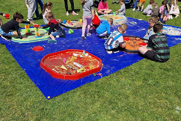 Young children play on a blue mat outdoors.