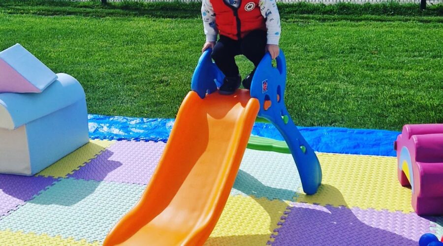 Young boy goes down an small orange slide.