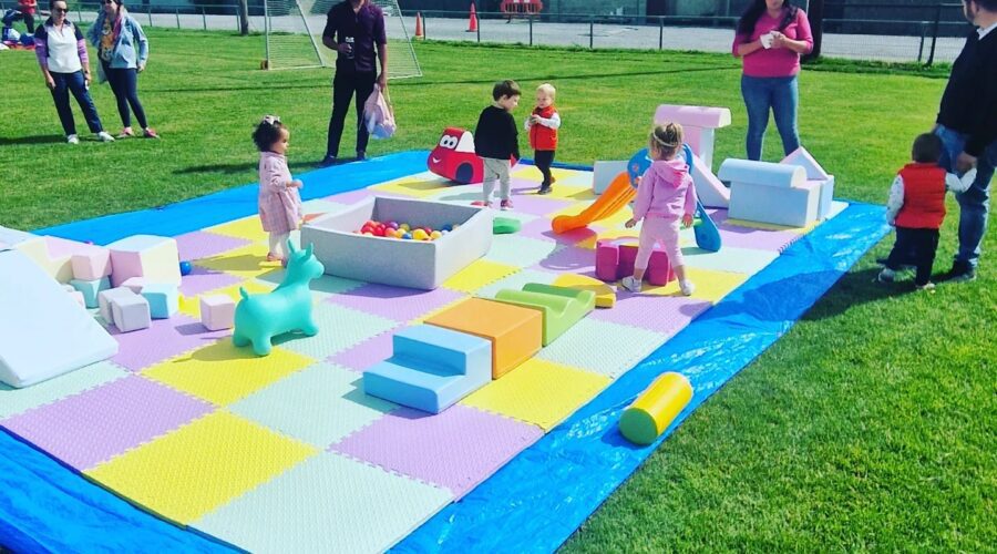 Children play on a large soft mat on a pitch.
