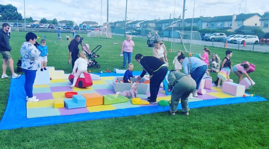Children play on a large soft mat on a pitch.