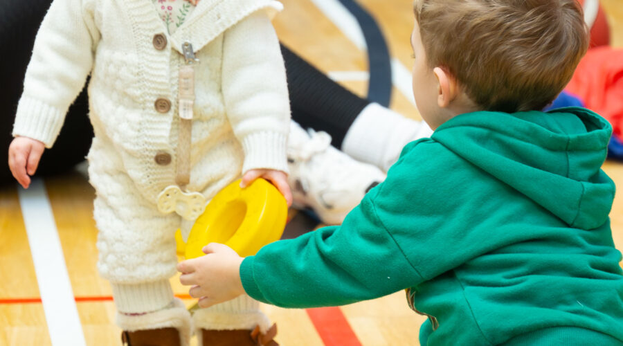 Two young children play on floor of gymnasium.