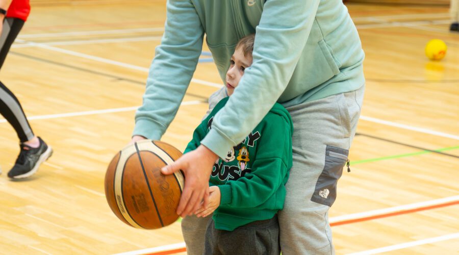 Man teaches young child how to throw a basketball.