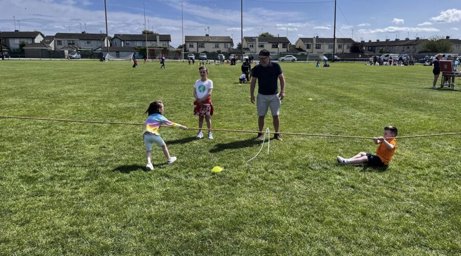 Young kids play tug of war on a pitch on a sunny day.