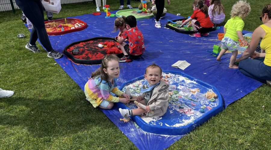 Young children play with sand on a mat on a pitch.