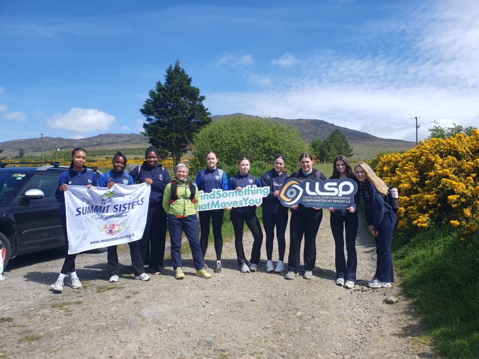 Group of teenage girls partake in summit sisters and stand with signage on a sunny day.